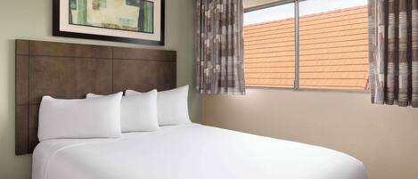 A neatly made bed with white linens, a dark headboard, and a framed picture above it.