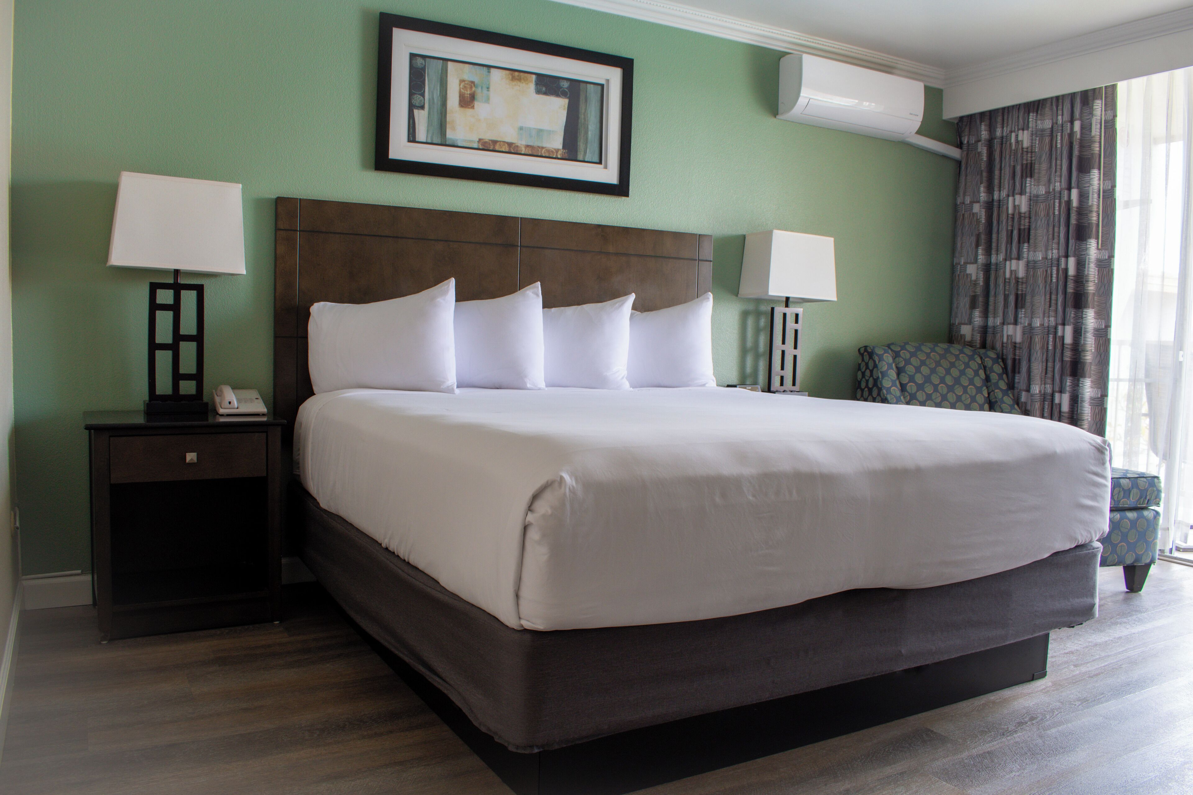 A hotel room with a large bed, two bedside tables, a chair, and a painting on the wall.