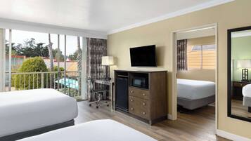 Een hotelkamer met twee bedden, een televisie, een bureau met een lamp en uitzicht op een zwembad en bomen.
