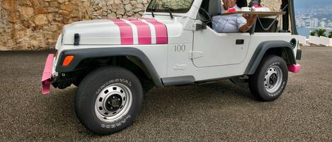 Un vehículo todoterreno blanco con detalles rosados estacionado frente a un muro de piedra.