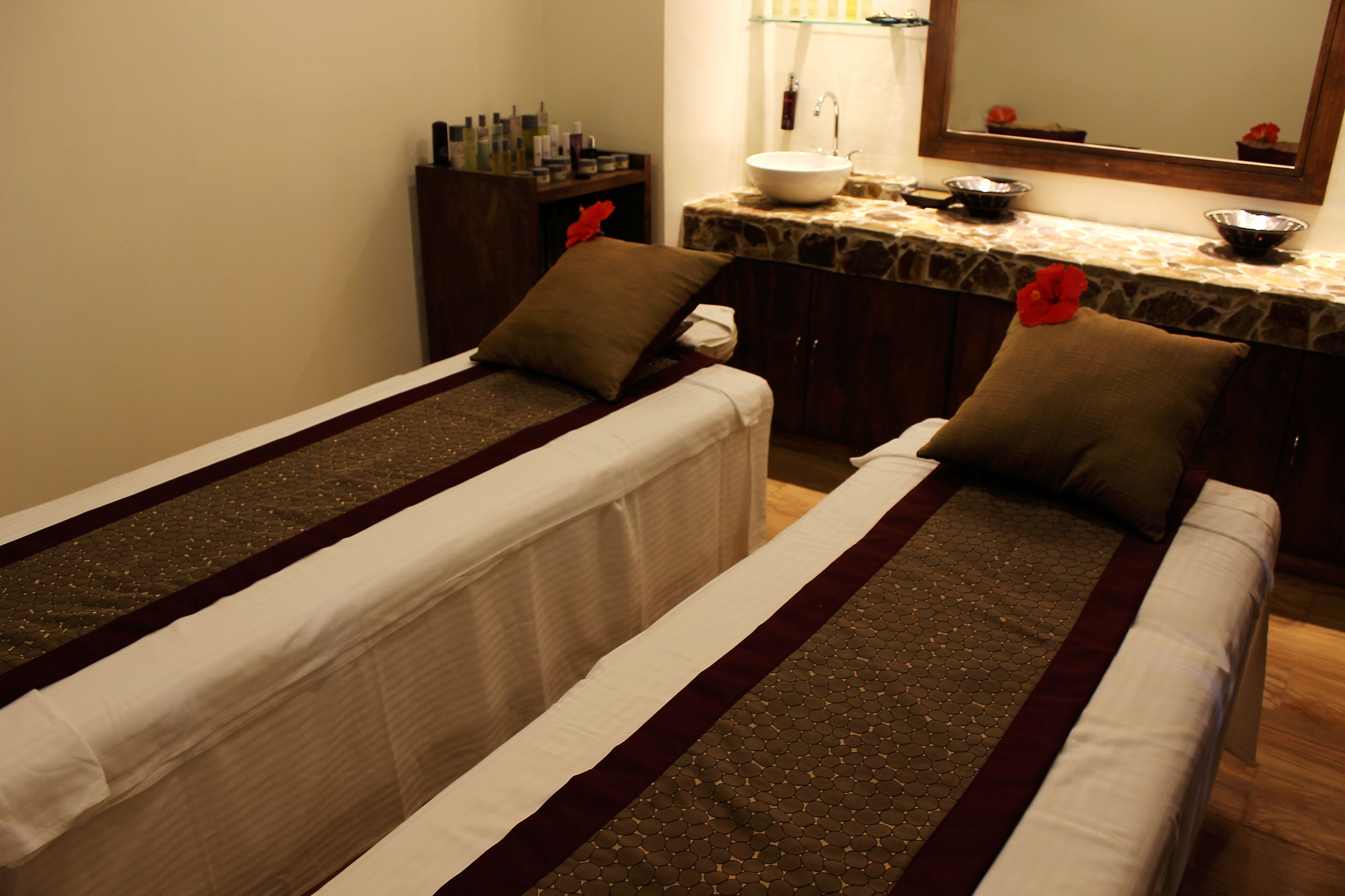 Quarto de hotel com duas camas, banheiro com pia e espelho, e amenities no balcão.