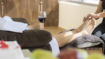 Una persona relajándose en un sofá con una copa de vino tinto, una toalla y una manta.