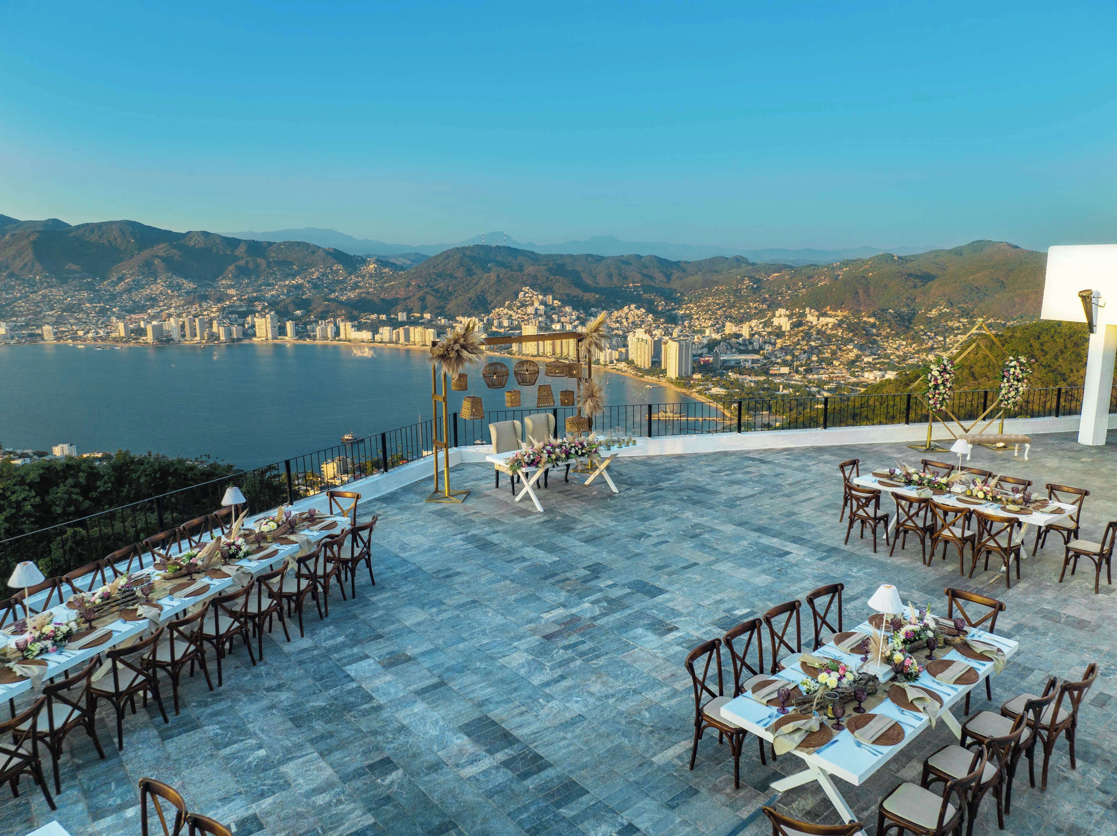 Un área de comedor al aire libre con mesas y sillas, con vista a una ciudad costera.