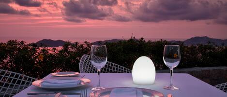 Una mesa para dos, con platos, cubiertos y vasos, con vistas a un paisaje escénico de montañas y atardecer.