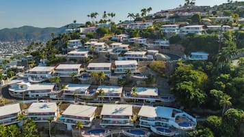 Zona residencial costera con varias casas de dos pisos, balcones, piscinas y abundante vegetación.