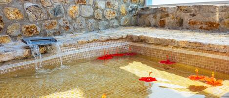 A stone wall with a tiled pool area containing water and red flowers.