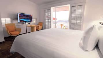 Habitación de hotel con una cama grande, televisión, una silla de mimbre, una mesita redonda y un balcón con vistas al agua.