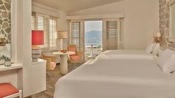 Habitación de hotel con una cama grande, una mesita redonda pequeña, una silla, una lámpara y vistas a las montañas.