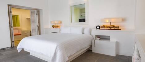 Habitación de hotel con una cama grande, mesitas de noche, un espejo y una puerta que da a un baño.