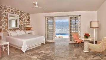 A hotel room with a bed, a desk, a TV, a chair, and a view of a pool and mountains.