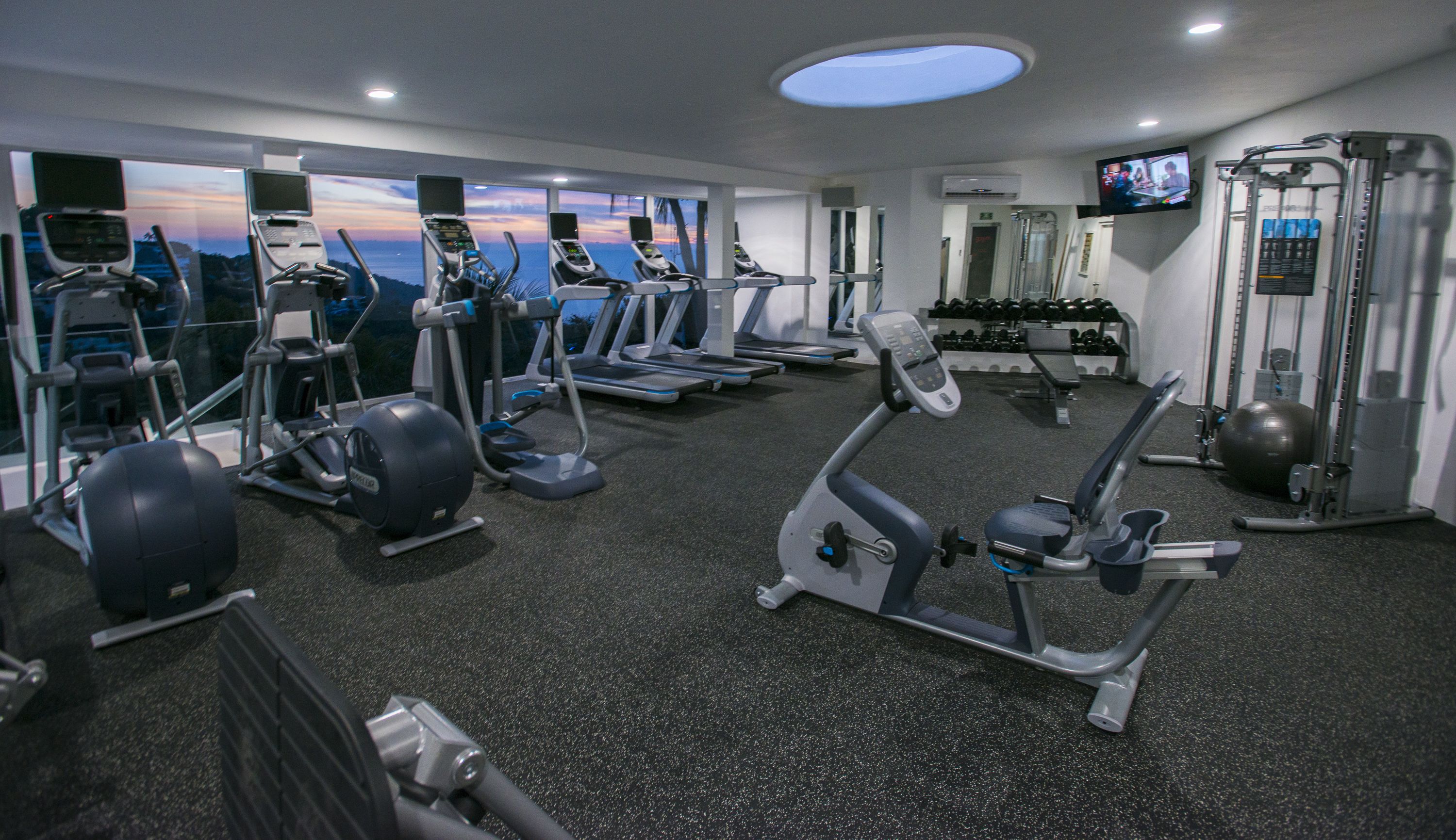 A gym with treadmills, weight machines, and a TV screen.