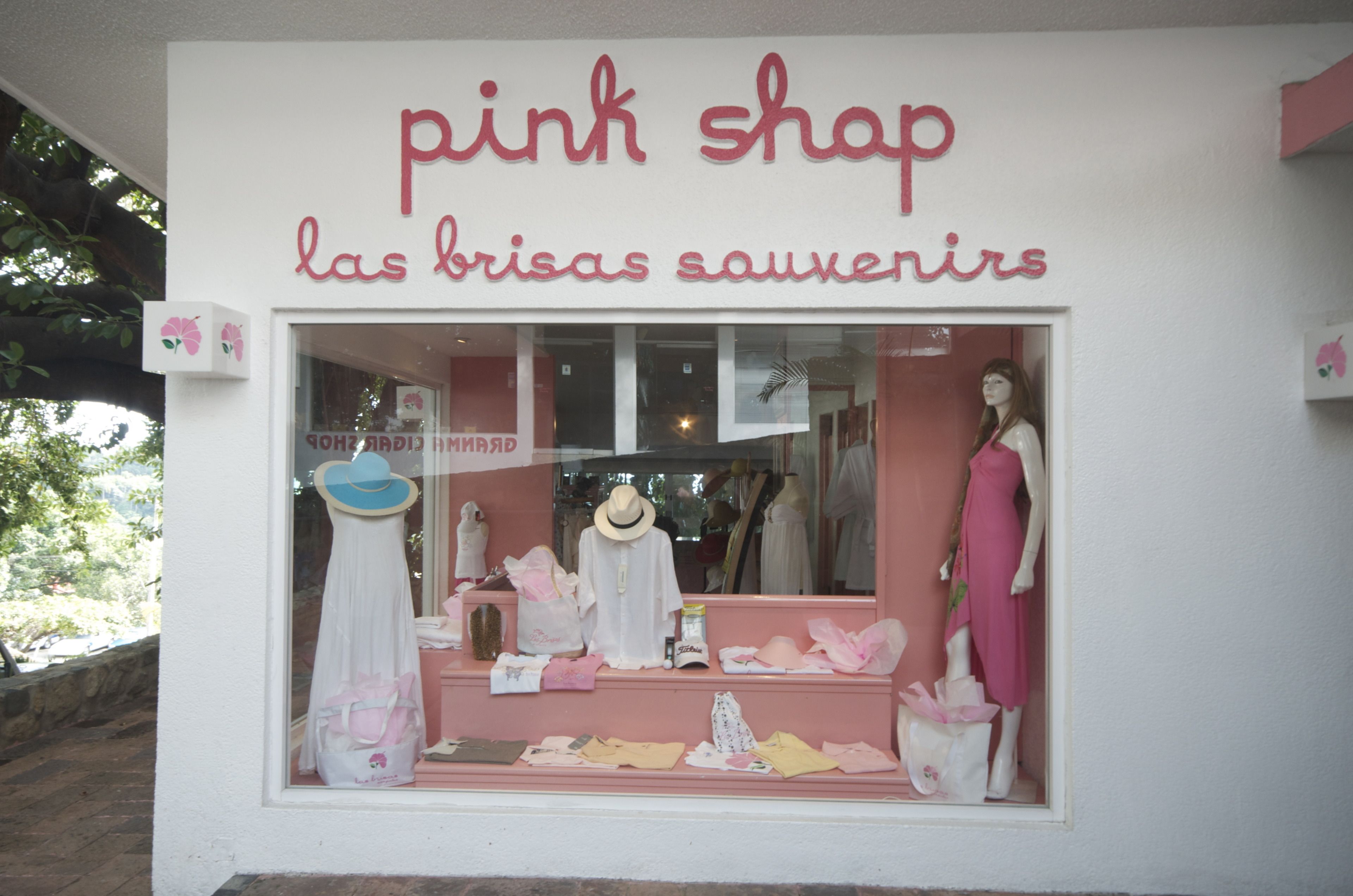 A storefront with a sign reading "pink shop las brisas souvenirs" and mannequins displaying clothing and accessories.