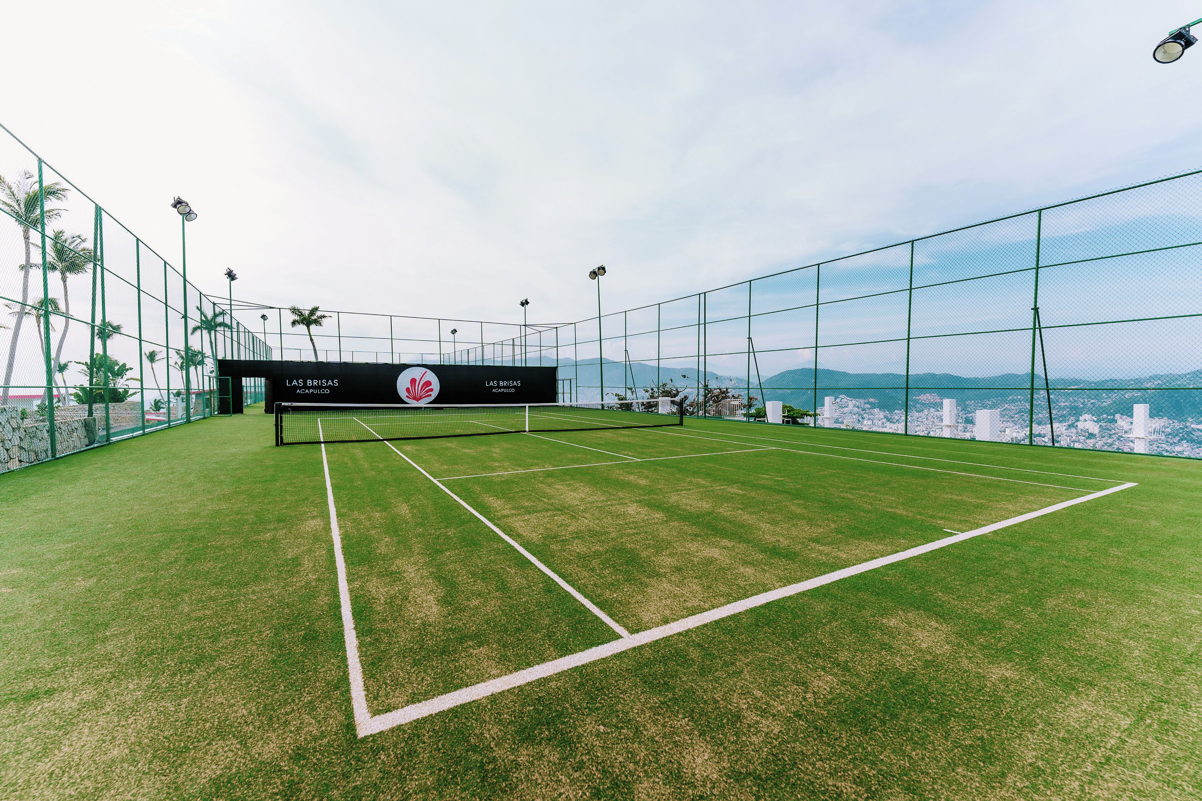 A tennis court with a net, surrounded by a fence, and a sign that reads "LAS BRISAS".