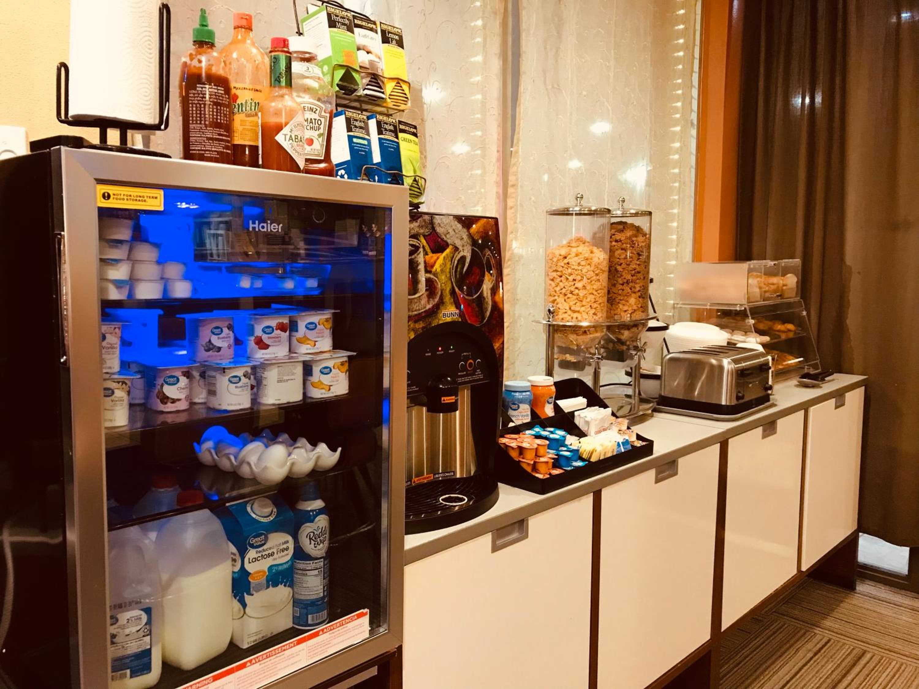 A self-service breakfast area with a vending machine, coffee machine, and a variety of food items.