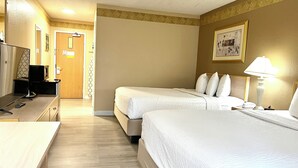 Ein Hotelzimmer mit zwei Betten, einem Schreibtisch, einem Fernseher und einer Lampe.