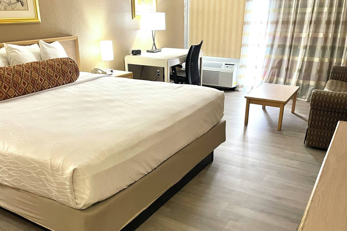 A hotel room with a large bed, bedside tables, a desk, a chair, and an air conditioning unit.
