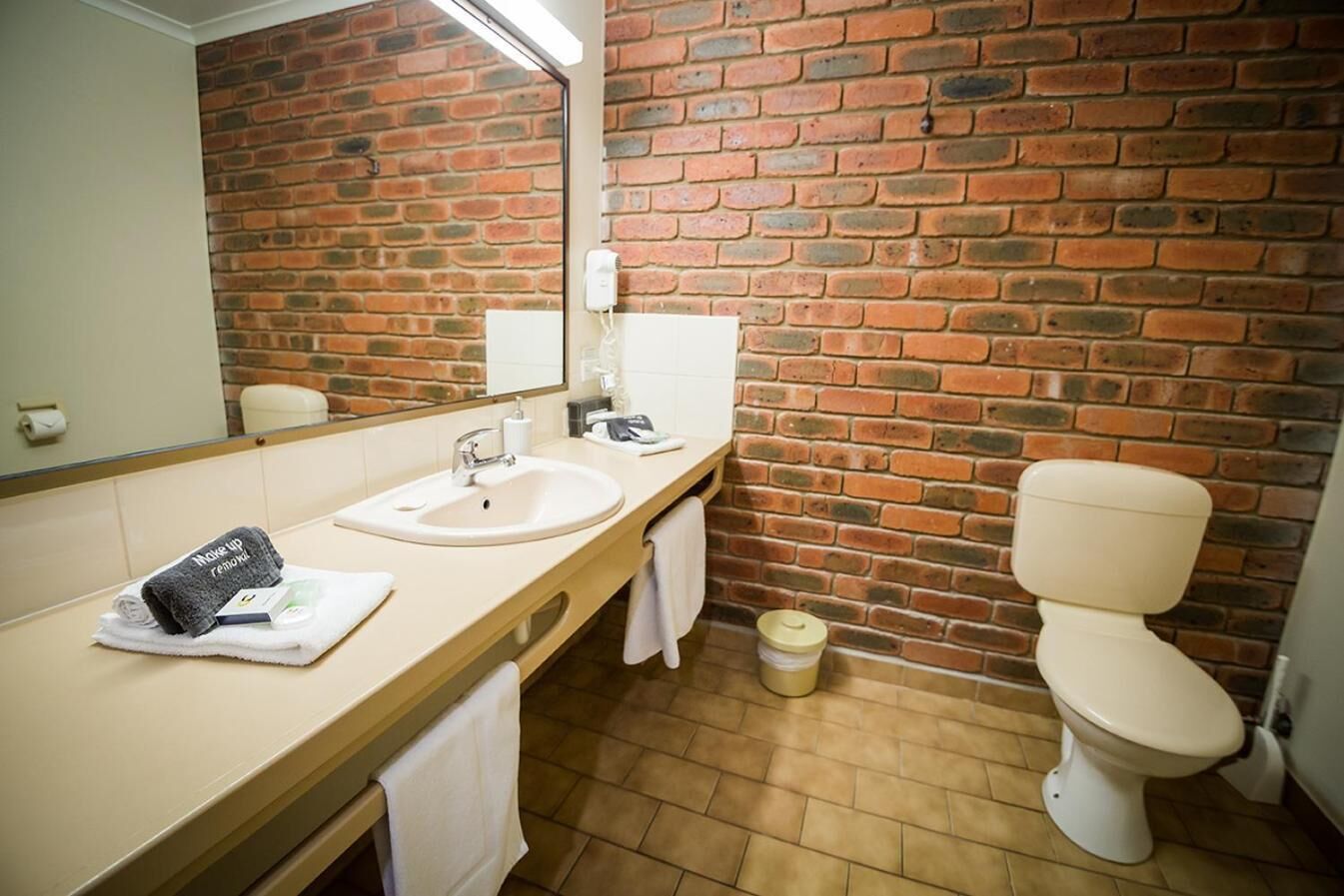 Une salle de bain avec un mur en briques, un lavabo, des toilettes et un miroir.