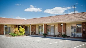 Un motel de dos pisos con techo de tejas, fachada de ladrillo y zona de estacionamiento cubierta.