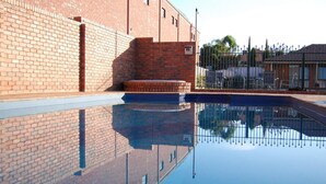 Una piscina con reflejo cristalino, un muro de ladrillo y una valla metálica al fondo.
