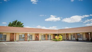 Un motel con techo de tejas, fachada de ladrillo y una zona de estacionamiento pavimentada.