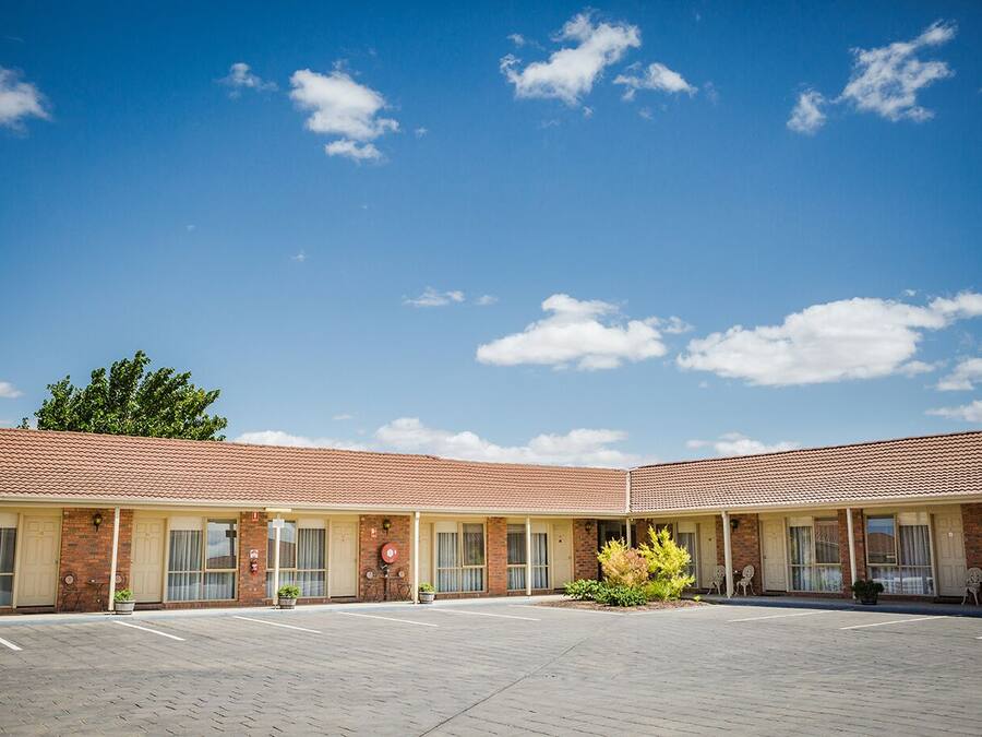 A motel with a tiled roof, brick facade, and a paved parking area.
