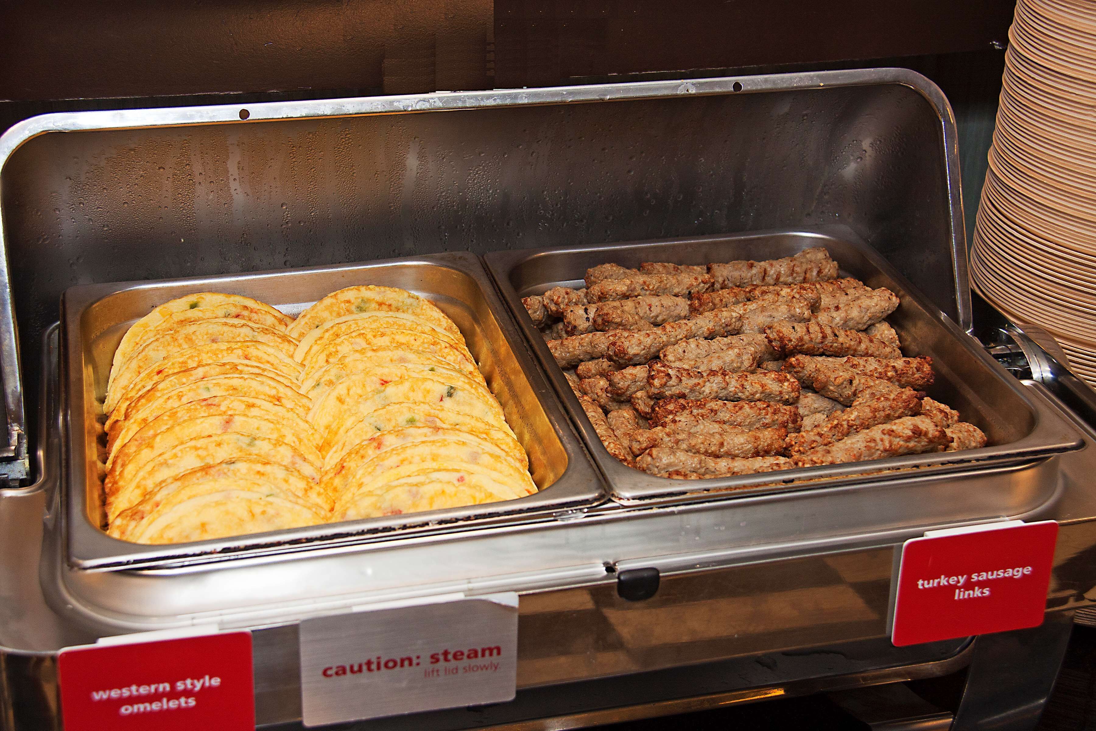 Een buffet met schalen vol westerse omeletten en kalkoenworstjes.