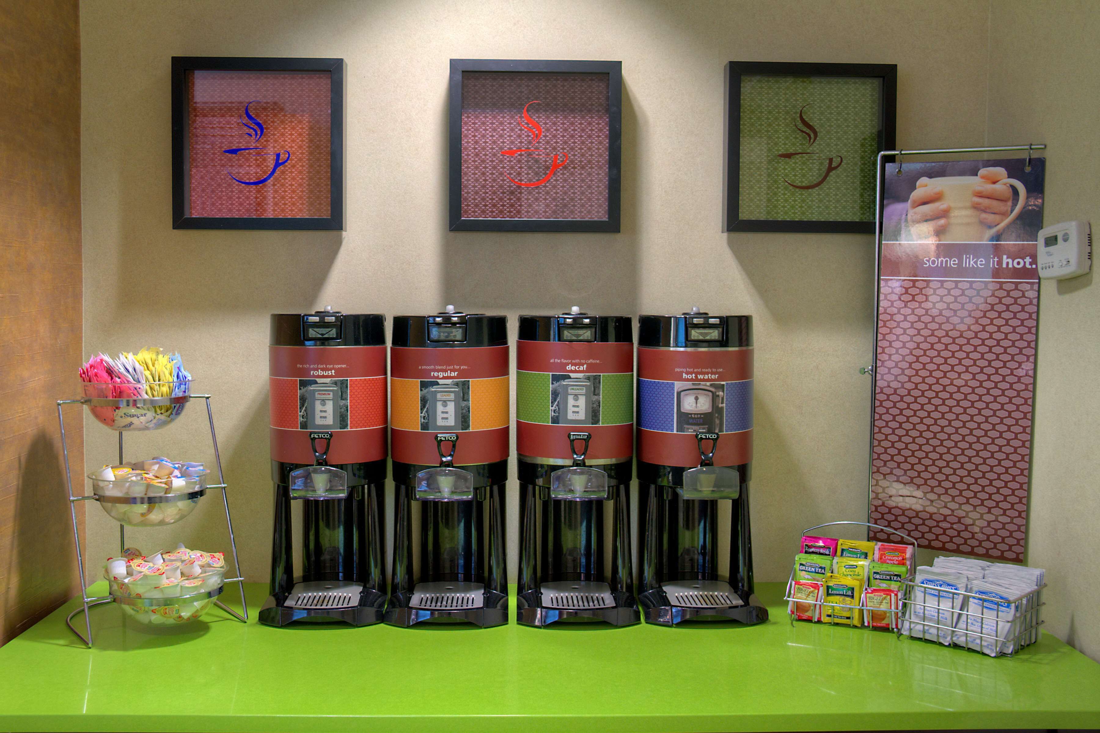 A coffee station with four dispensers labeled regular, decaf, and hot water, and a basket of napkins.