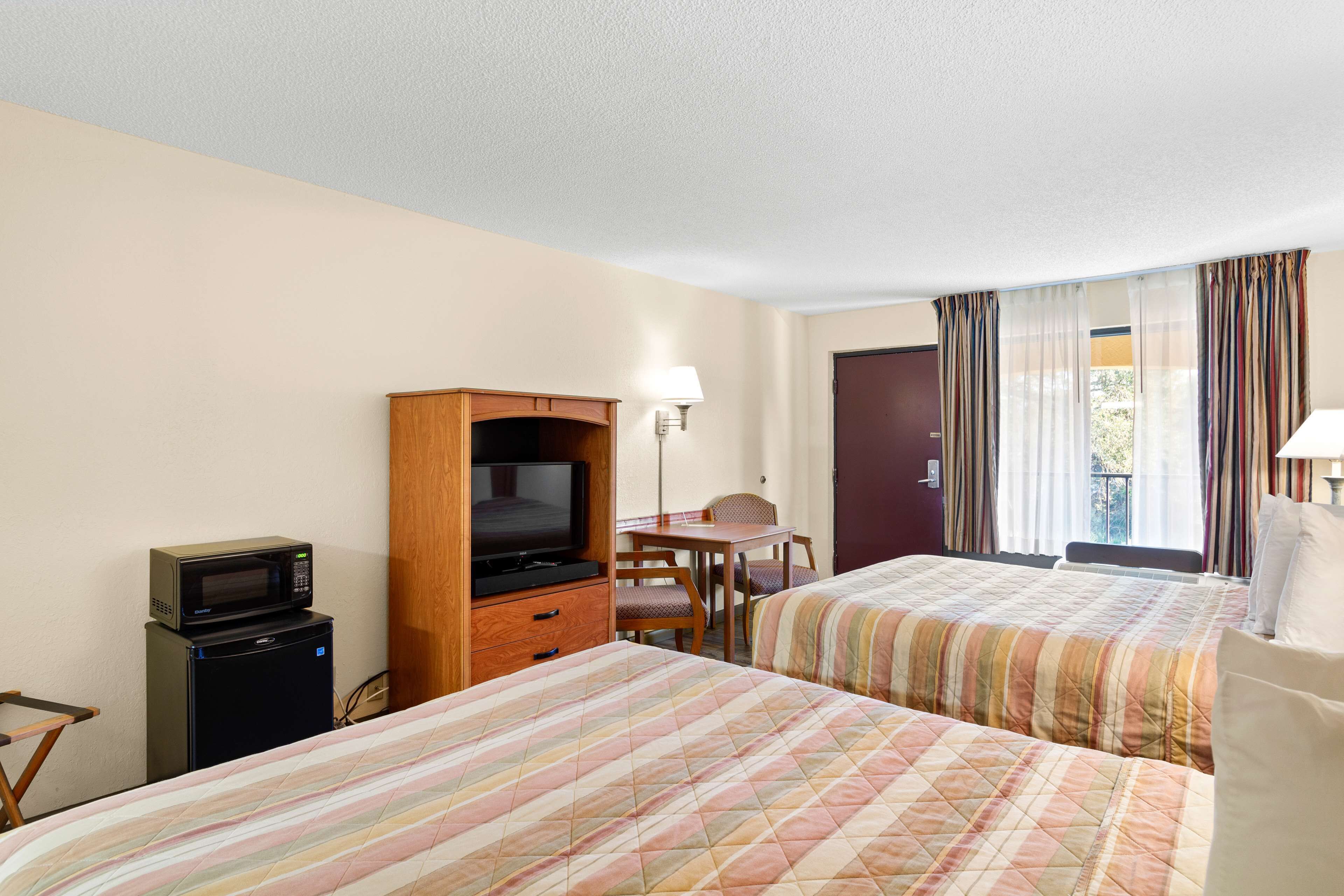 Habitación de hotel con dos camas, televisión, refrigerador pequeño, escritorio y una silla.