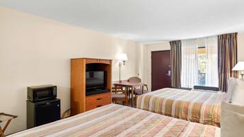 Habitación de hotel con dos camas, televisión, refrigerador pequeño, escritorio y una silla.