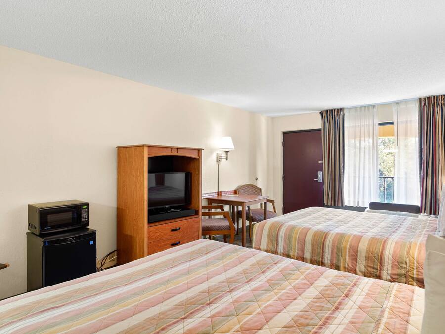 Habitación de hotel con dos camas, televisión, refrigerador pequeño, escritorio y una silla.