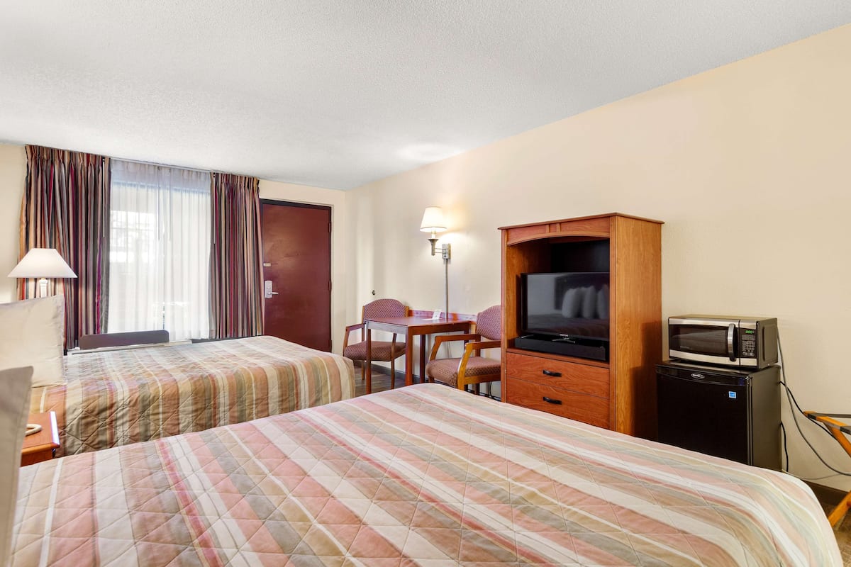 A hotel room with two beds, a desk, a television, and a microwave.