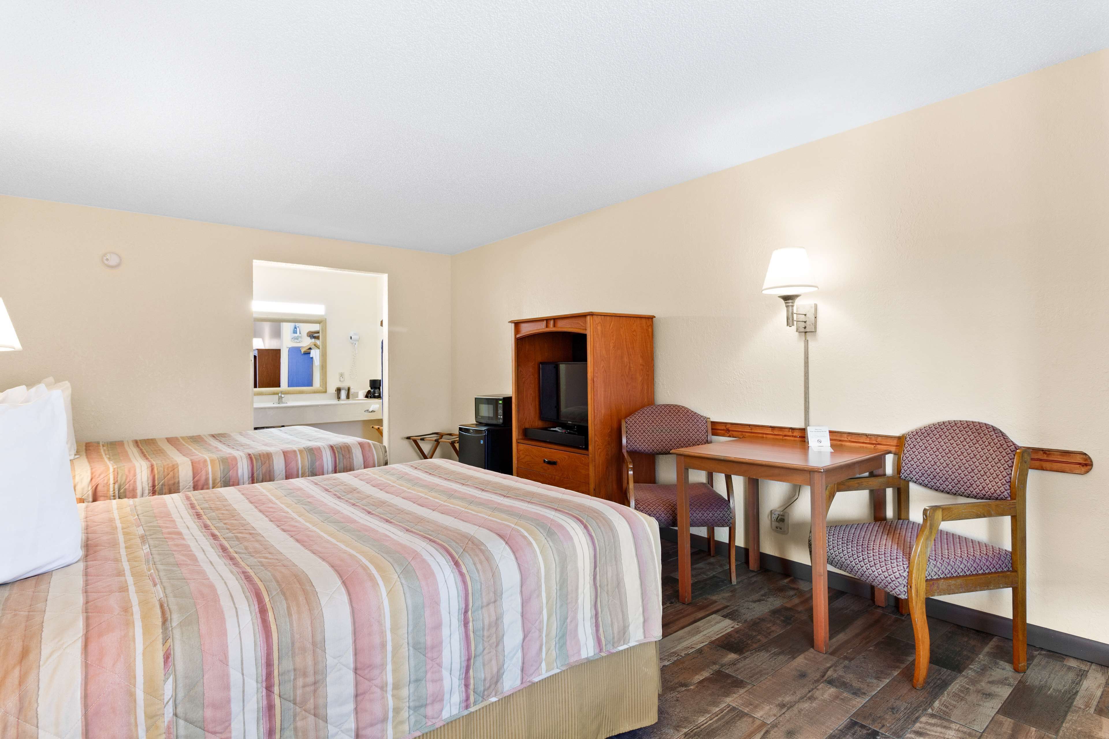 Ein Hotelzimmer mit zwei Betten, einem Schreibtisch, einem Stuhl, einem Fernseher und einer Lampe.
