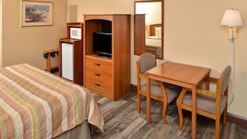 Ein Hotelzimmer mit einem Bett, einem Schreibtisch mit Stuhl, einem Fernseher, einem Schminktisch und einem Spiegel.