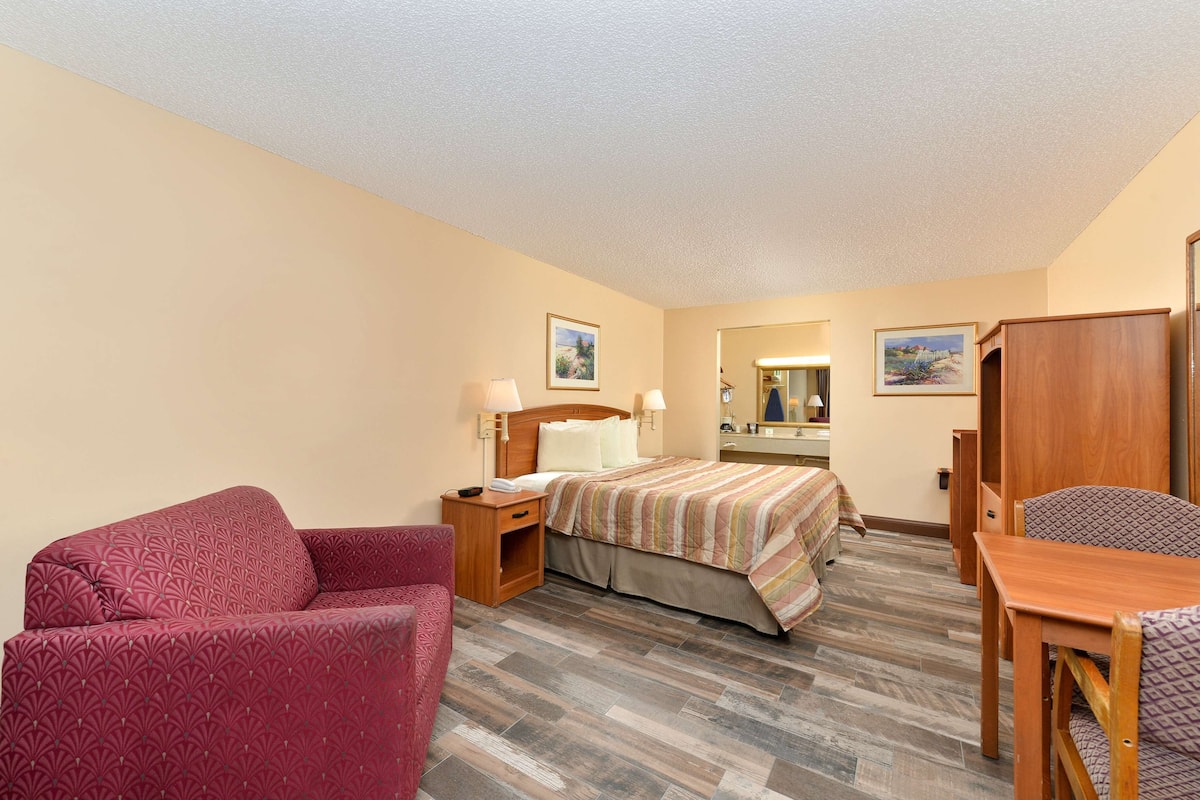 A hotel room with a bed, a desk, a chair, a nightstand, and a wardrobe.