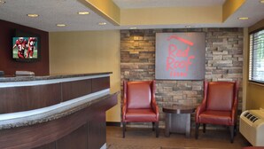 A reception area with a counter, two leather chairs, a small table, a fireplace, and a television mounted on the wall. - Red Roof Inn Elkhart (Elkhart)