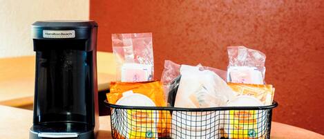 A coffee maker and a basket of packaged food items on a countertop.