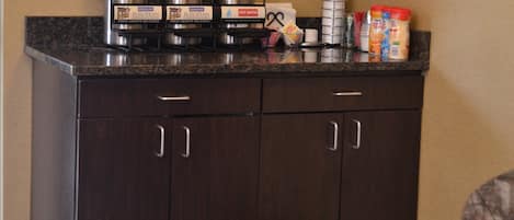 A kitchenette with a coffee maker, a kettle, and a hot water dispenser. There are also condiments and a coffee mug on the counter.