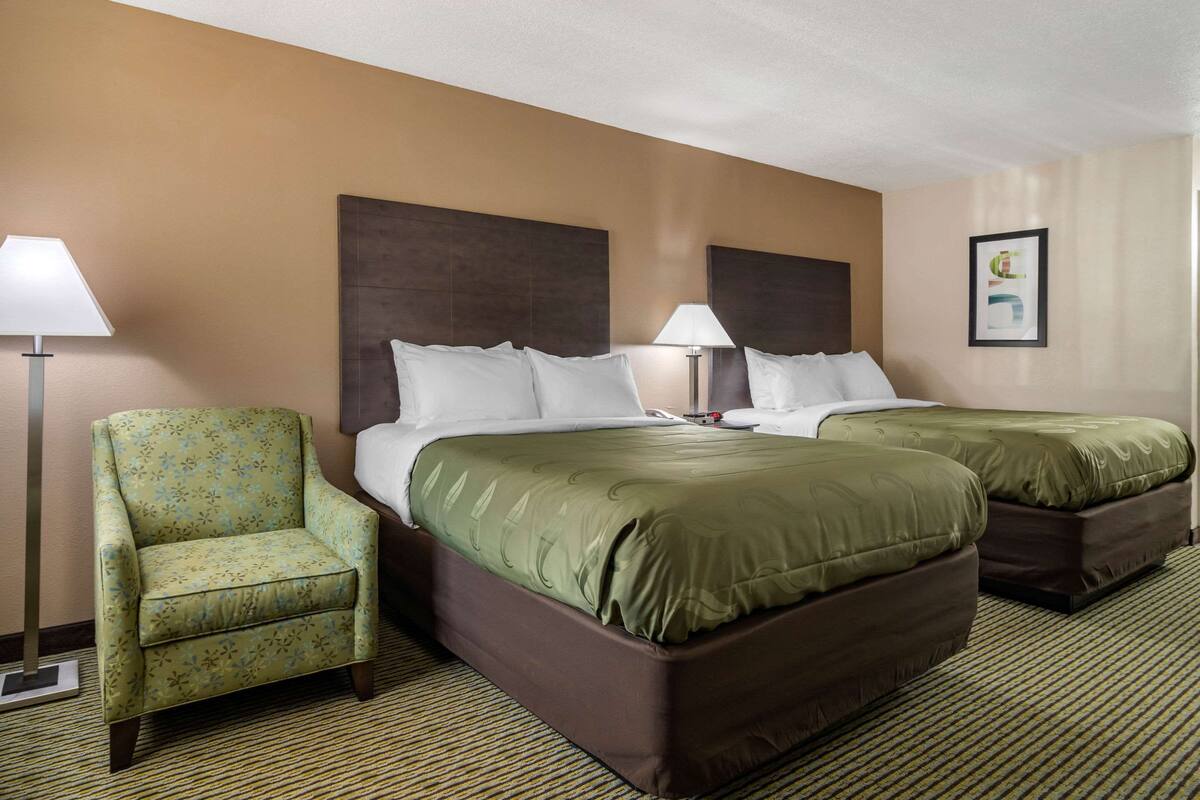 A hotel room with two beds, a chair, a lamp, and a framed picture on the wall.