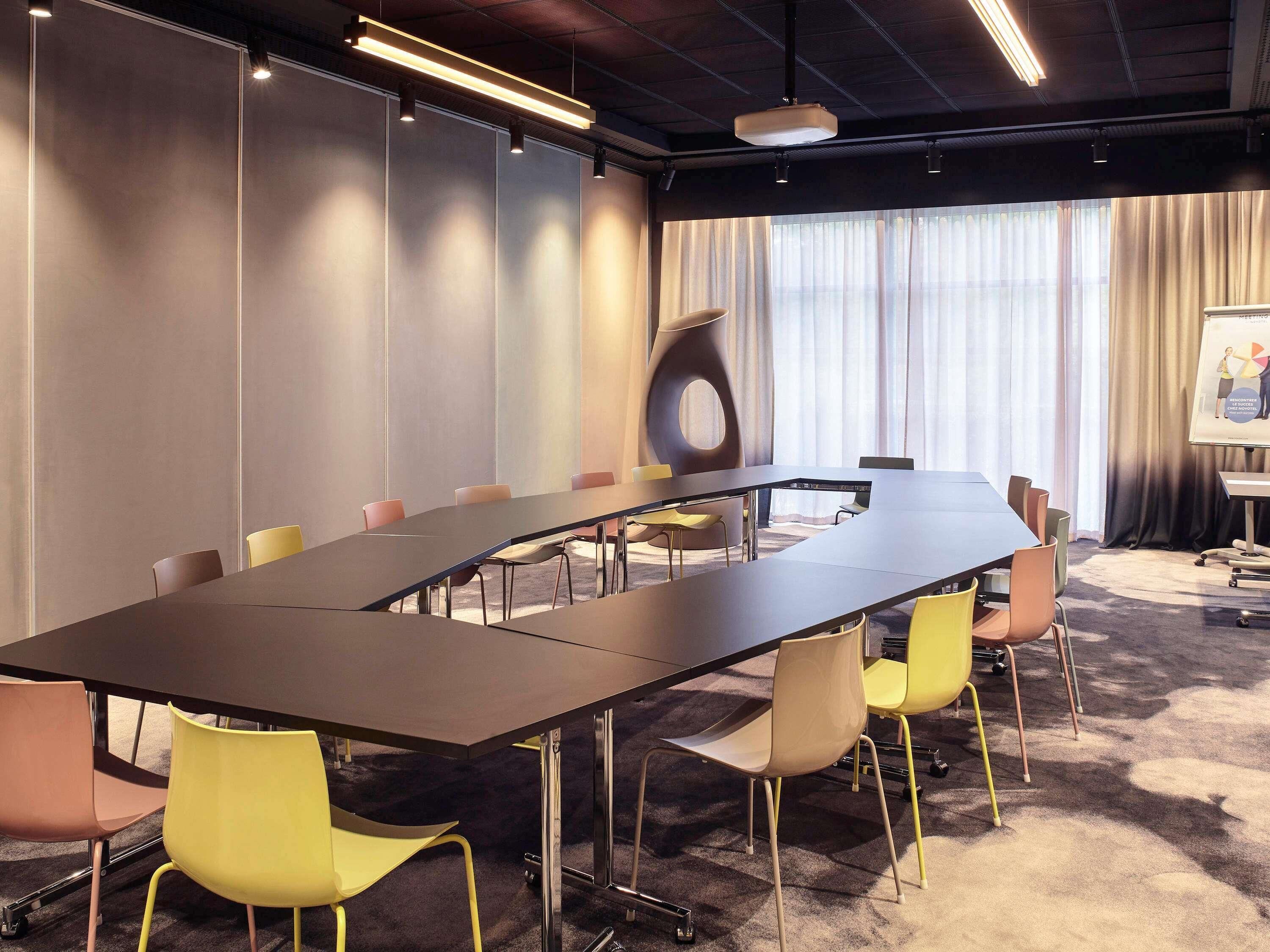 A conference room with a long table, chairs, a projector screen, and a large window with curtains.