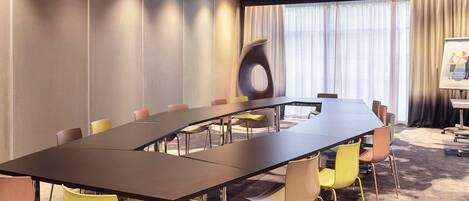 A conference room with a long table, chairs, a projector screen, and a large window with curtains.