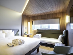 Ein Hotelzimmer mit einem großen Bett, einem kleineren Bett, einem Sessel, einem Nachttisch, einem Spiegel und einem Fenster mit Blick.
