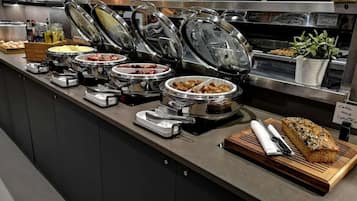 A buffet setup with various food items and a loaf of bread on a wooden board.