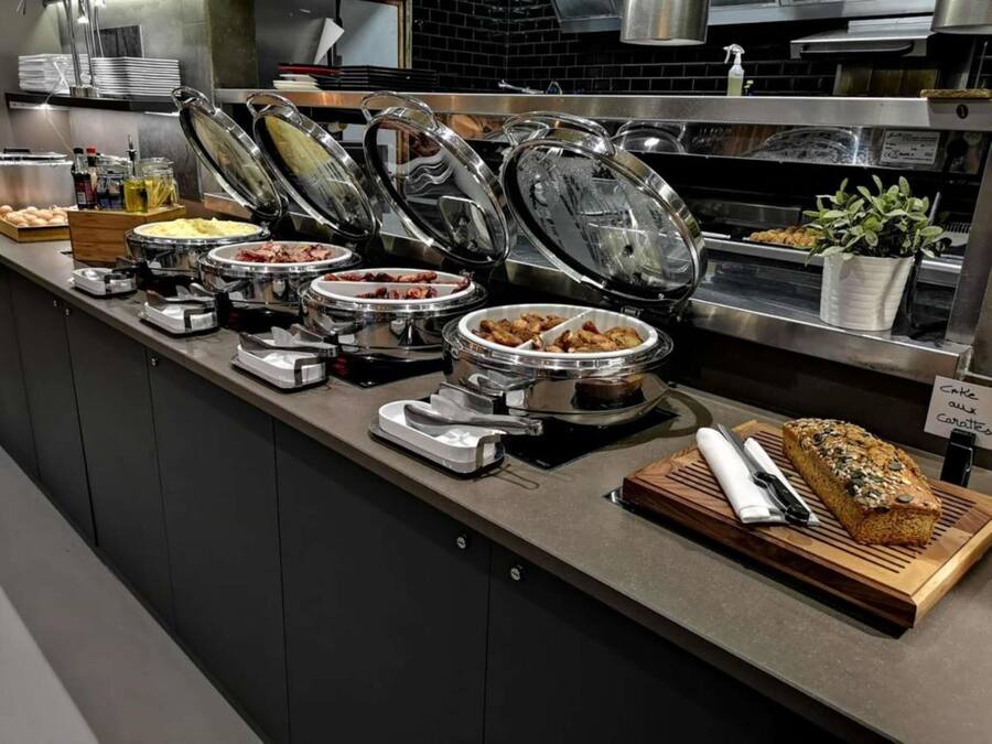 A buffet setup with various food items and a loaf of bread on a wooden board.