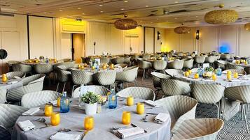 A banquet hall with round tables, cushioned chairs, and hanging spherical light fixtures.