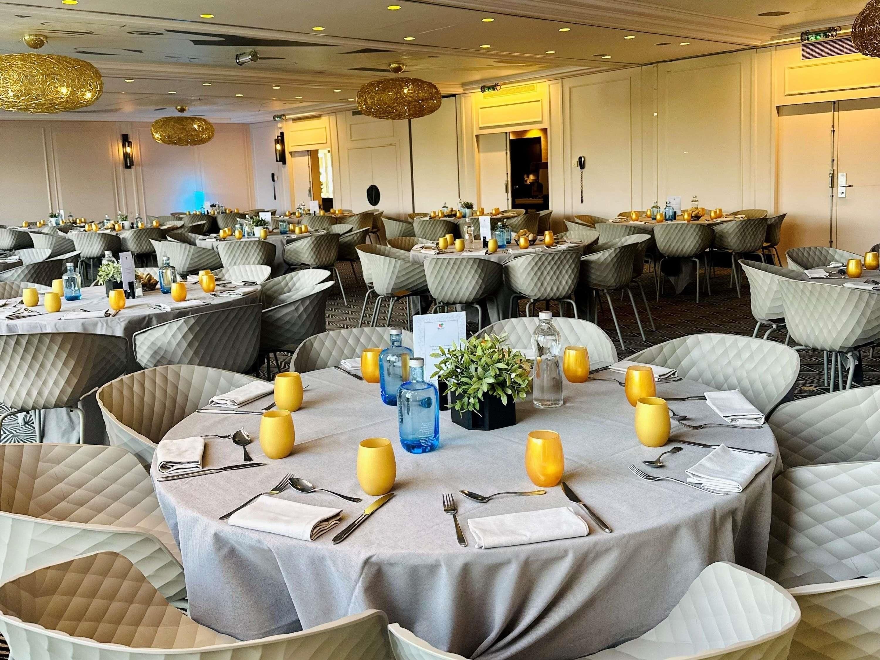 A banquet hall with round tables, grey upholstered chairs, and yellow candle holders.