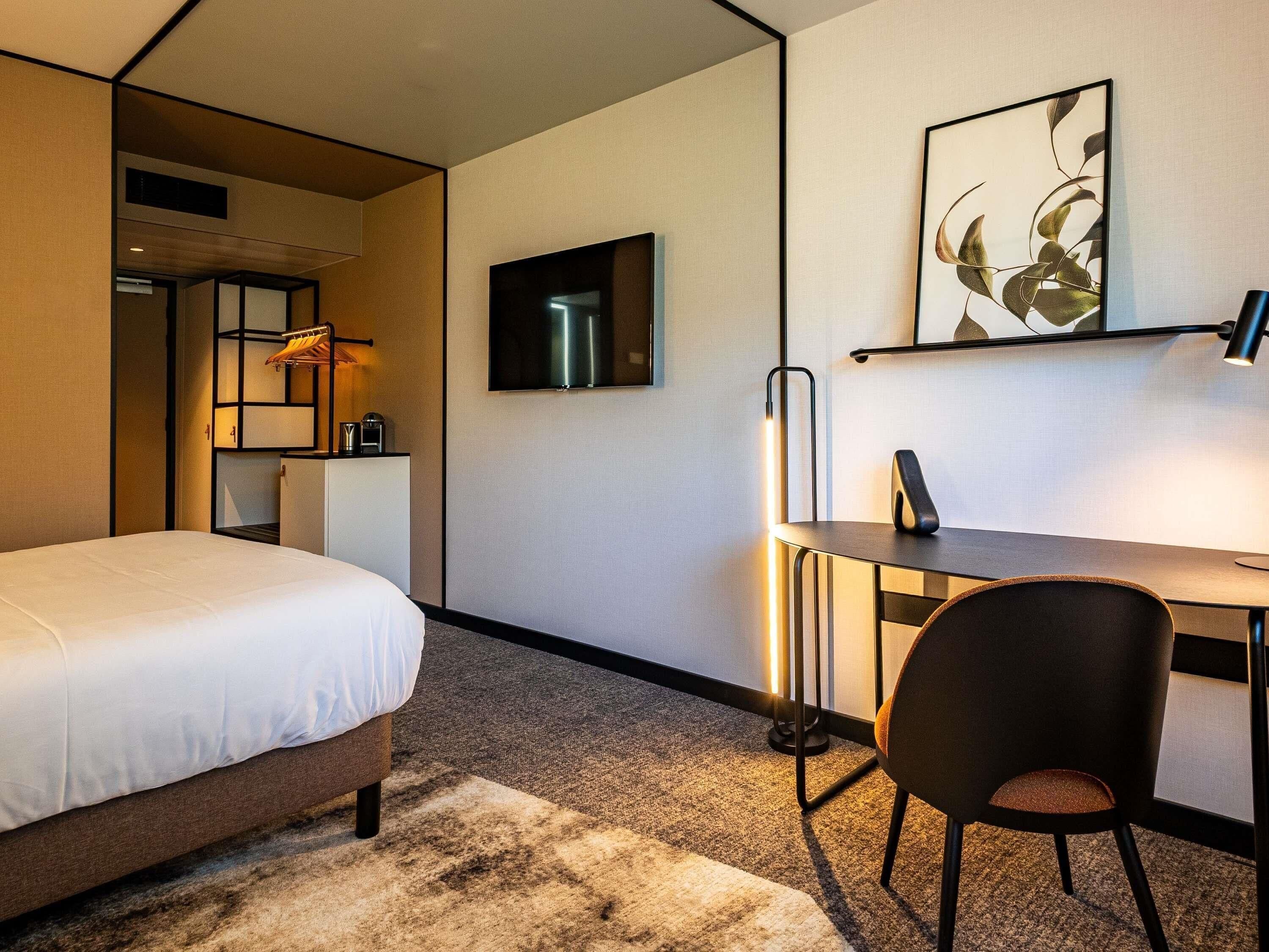 Ein Hotelzimmer mit Bett, Schreibtisch, Stuhl und Fernseher.