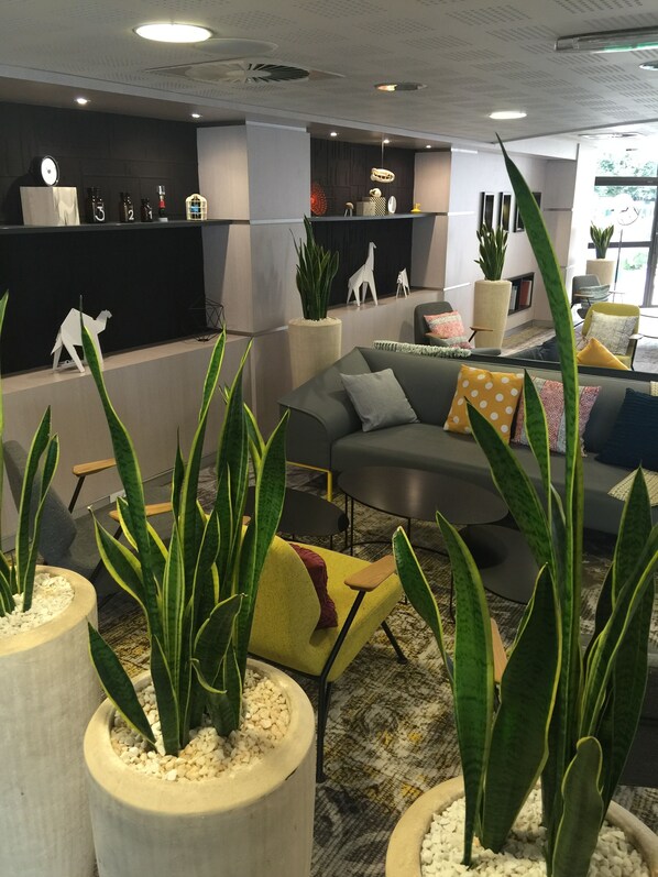 A modern interior with a sofa, potted plants, and a decorative wall. - Novotel Marne Vallee Collegien (Collegien)