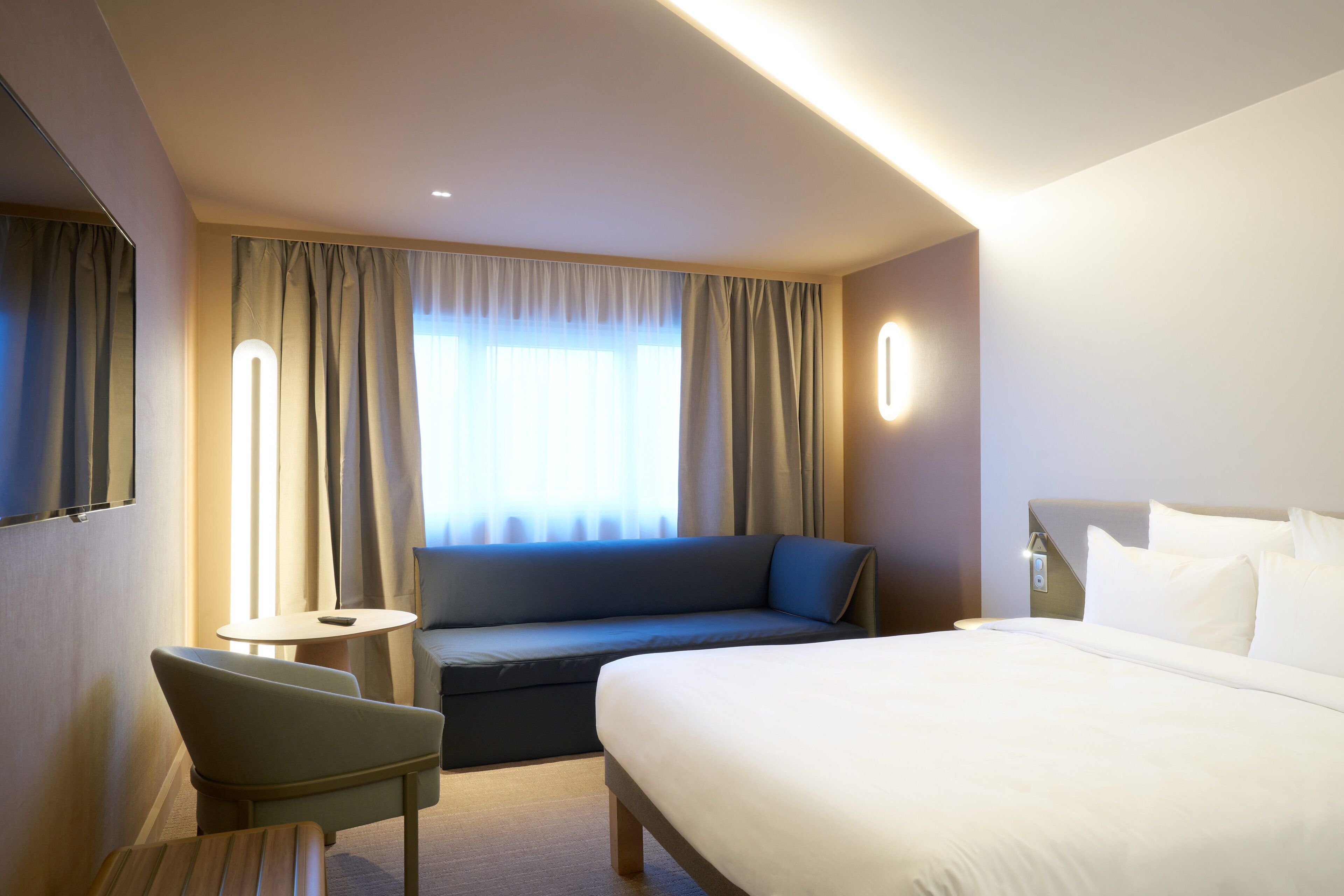Ein Hotelzimmer mit einem Bett, einer Couch, einem kleinen Tisch und einem Fernseher an der Wand.