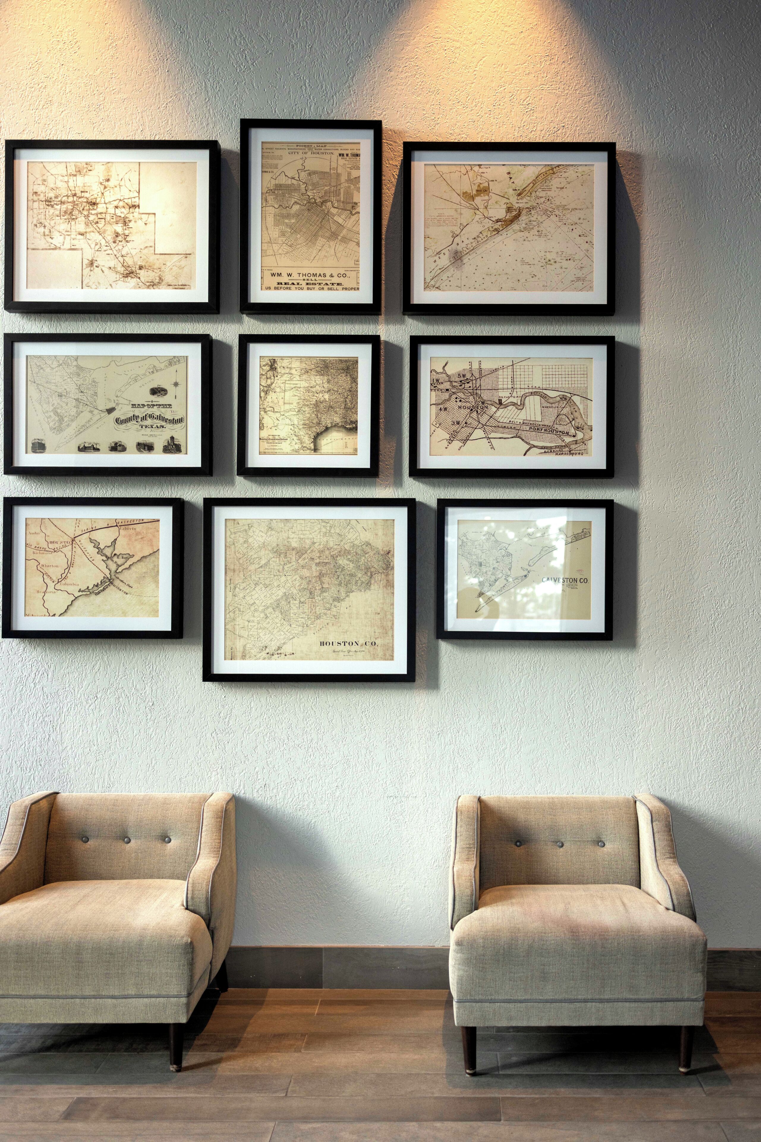 A wall with framed maps and two upholstered chairs.