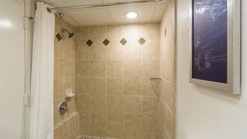 Una ducha con azulejos color beige, un cabezal de ducha y un dispensador de jabón.